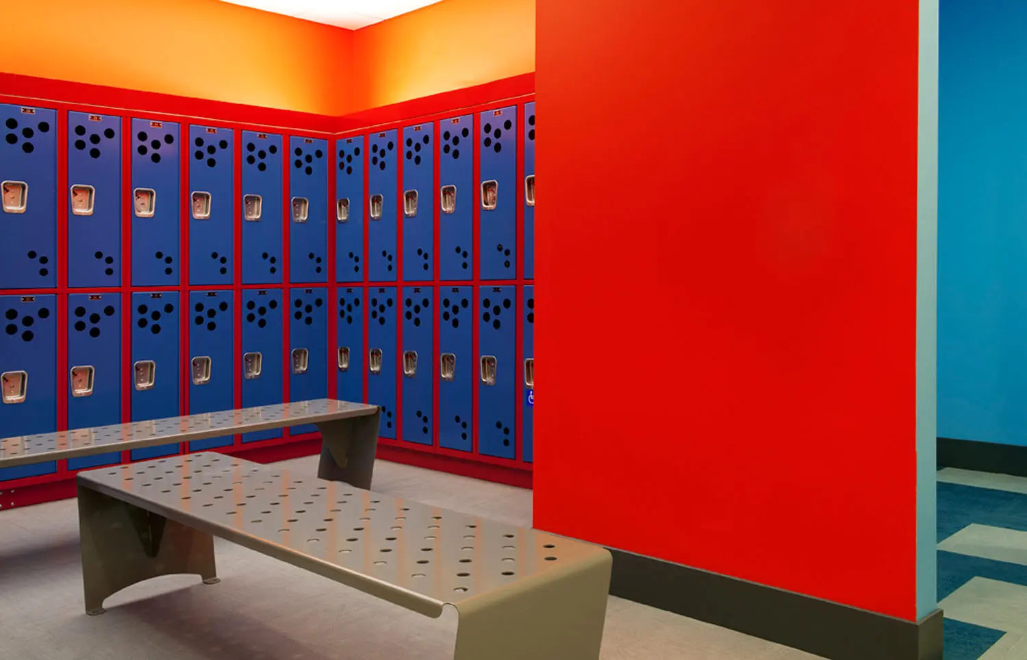 A room with blue and red lockers, a bench and a wall.